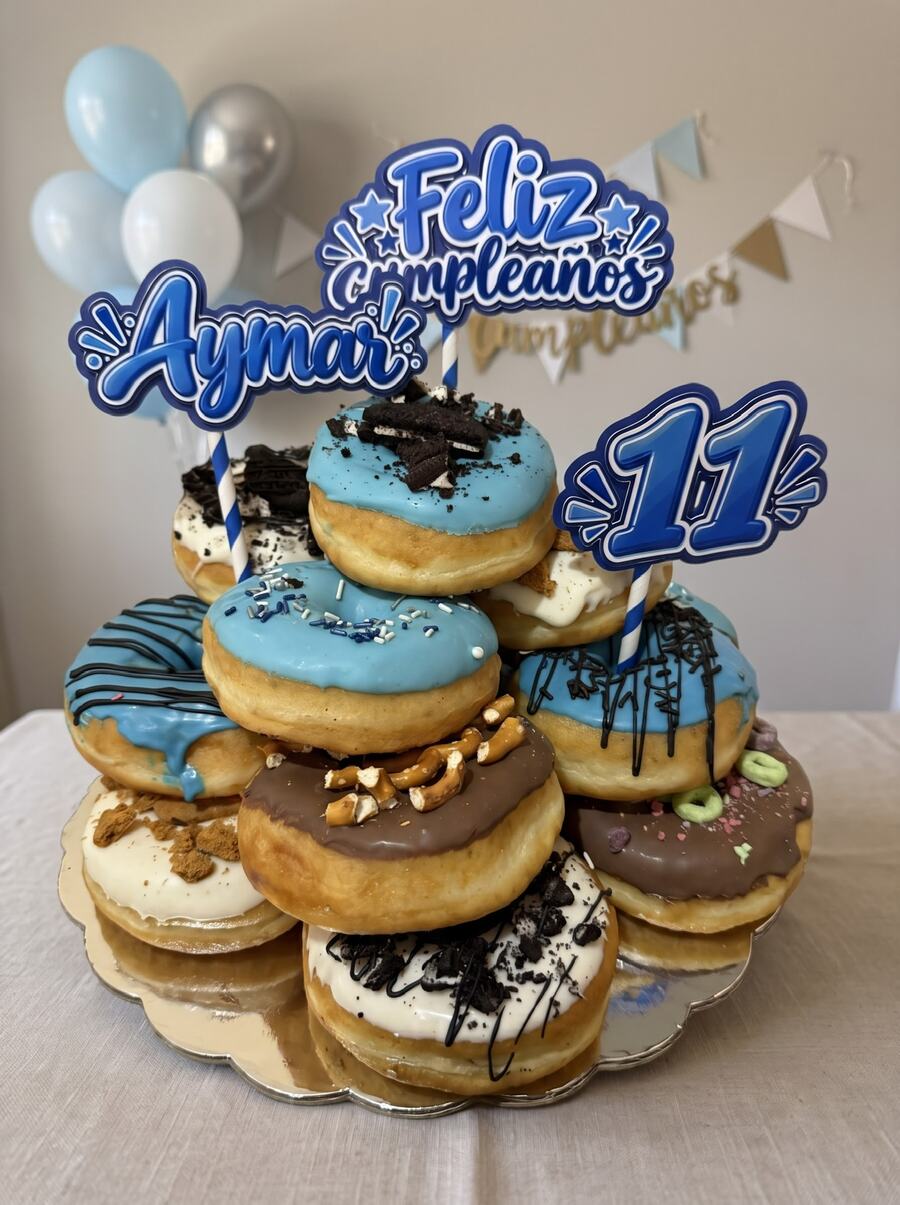 Pastel de donas azul con toppings de Oreo, pretzels y cereal, con cake toppers personalizados de cumpleaños